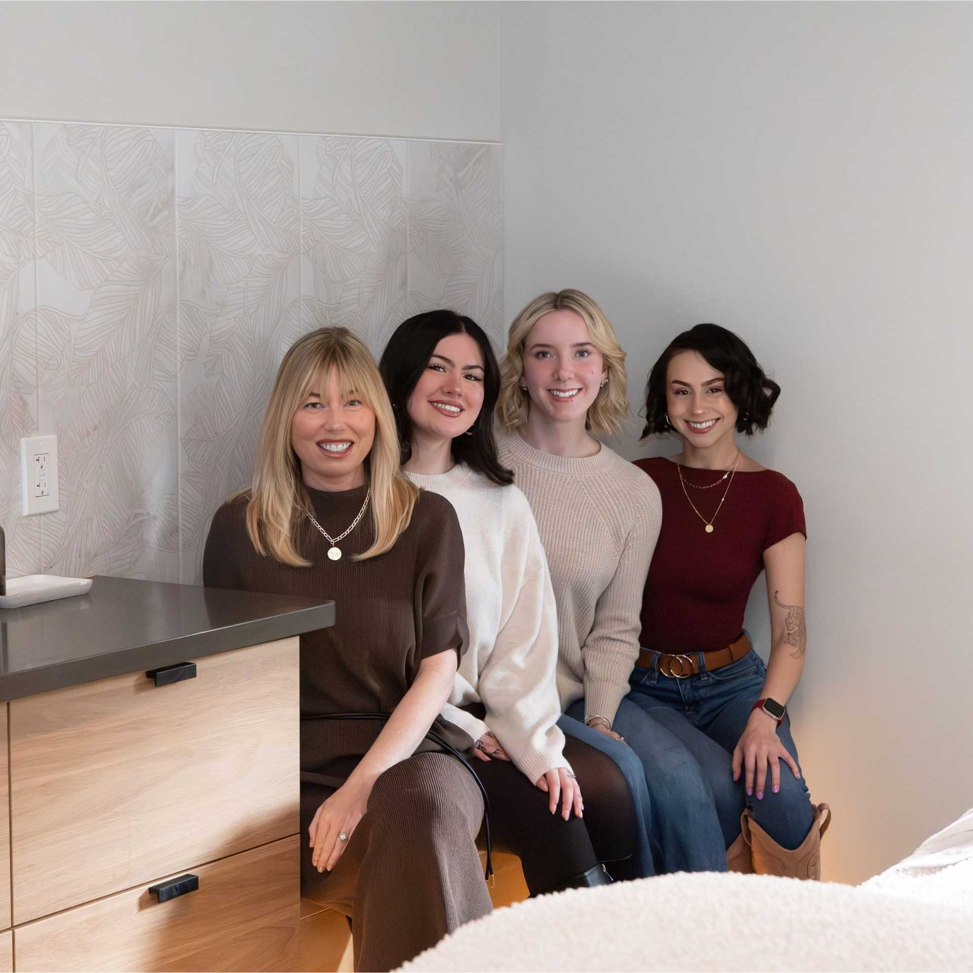 Group of four women sitting together, smiling in a cozy indoor setting.